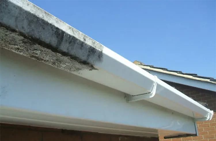 White fascia and soffit with dark staining beside a cleaned section