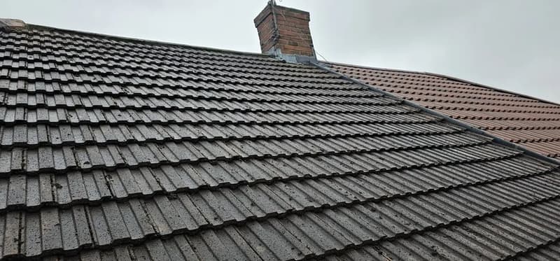 Grey tiled roof with little visible moss and a brick chimney
